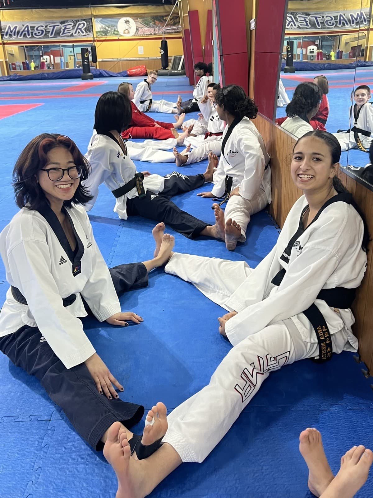 Students in white uniforms sitting and stretching together on the blue training mats