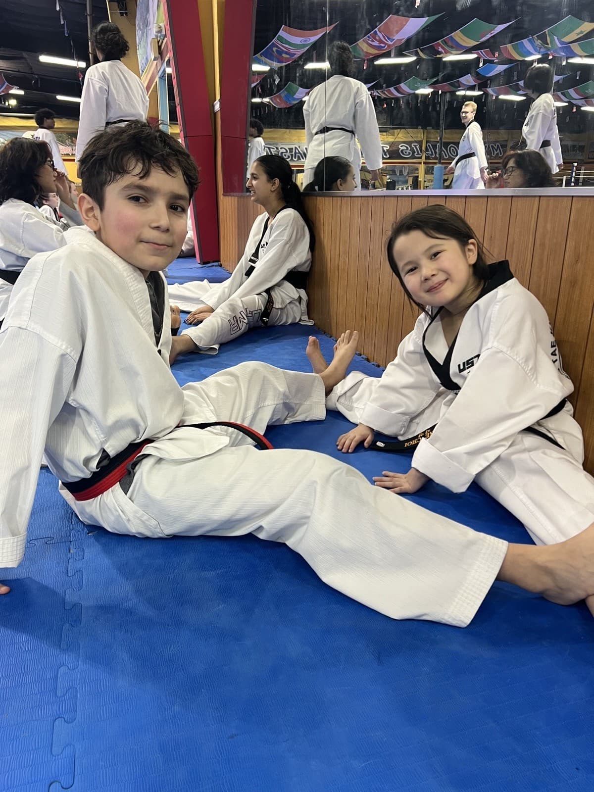 Two young USTMA students in uniform sitting on the training mat, smiling