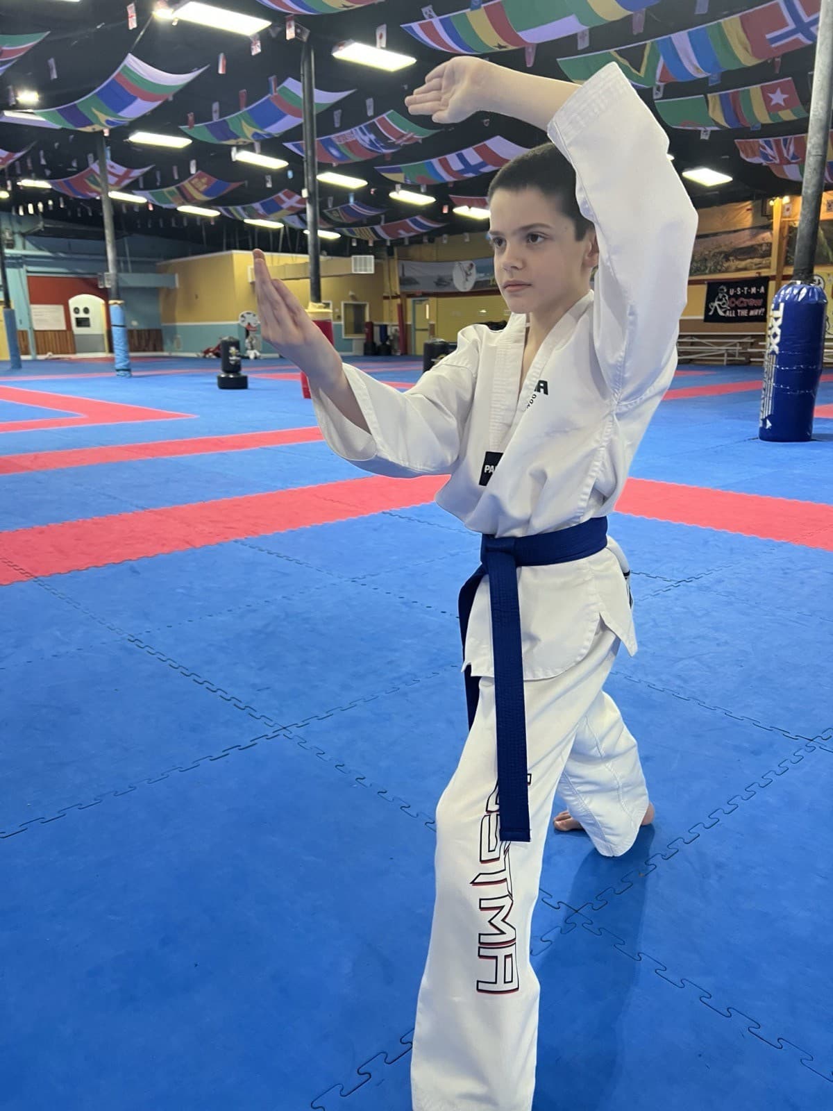 A young student with a blue belt holding a stance on the training mat