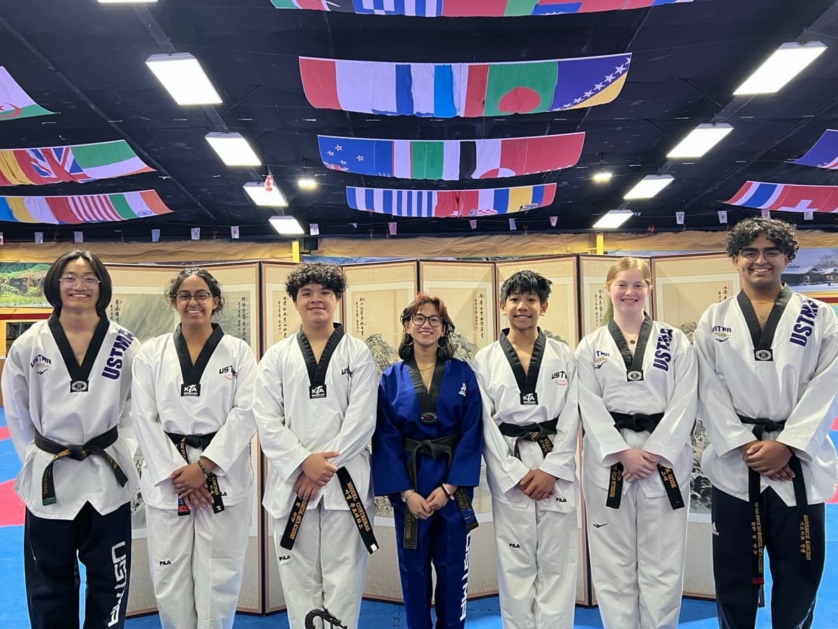 Seven students in uniform with black belts standing in a row in the training hall